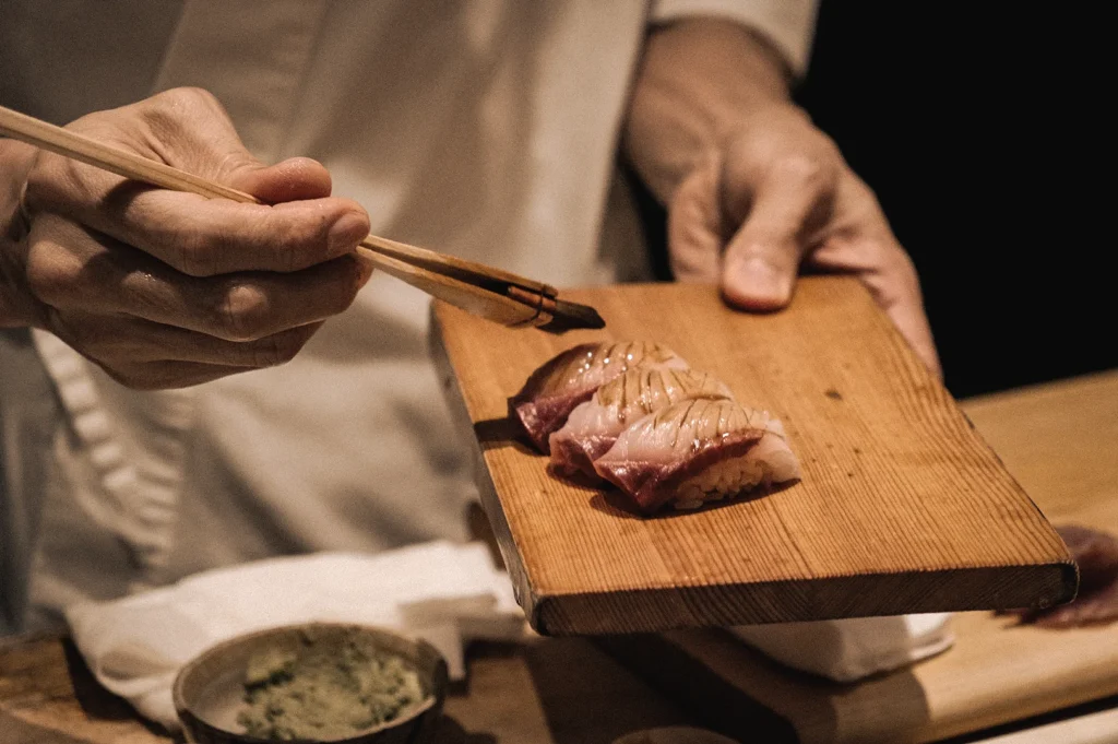Close-up high-angle shot of a chef glazing fresh nigiri sushi on a wooden serving board at Sushi to Sumi standing sushi bar in Raffles Place, Singapore CBD