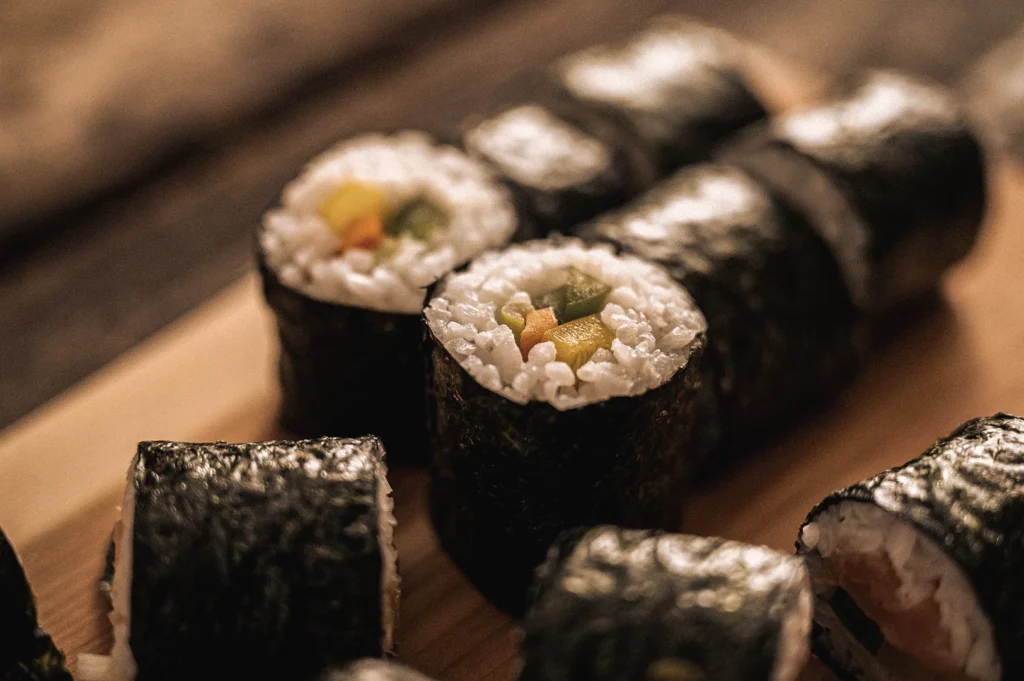 Close-up macro view of traditional maki sushi rolls arranged on a wooden serving board, featuring nori-wrapped vinegared rice filled with fresh vegetables, showcasing authentic Japanese rolled sushi and makizushi preparation.