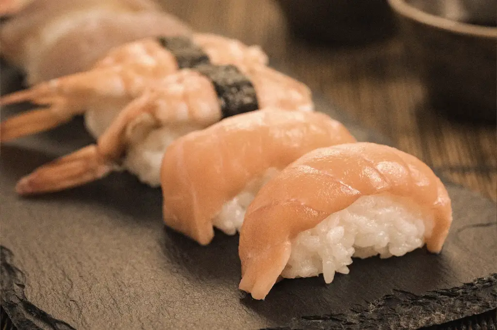 Eye-level macro close-up of freshly prepared salmon nigiri and shrimp nigiri arranged on a black slate serving board, highlighting premium seafood, vinegared sushi rice, and traditional Japanese sushi craftsmanship.
