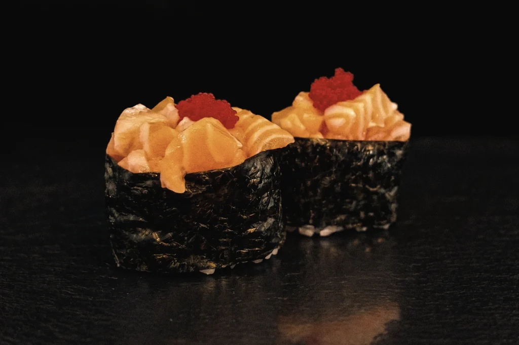 Premium gunkan sushi topped with diced salmon and bright salmon roe, wrapped in crisp nori and photographed from a low-angle macro perspective to highlight the signature battleship sushi shape and rich seafood topping.