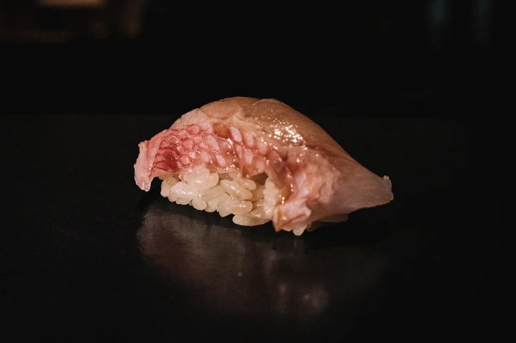 Low-angle macro photograph of a single nigiri sushi piece with delicately sliced fish over seasoned sushi rice, illustrating what nigiri sushi is and the precision of Japanese sushi preparation.