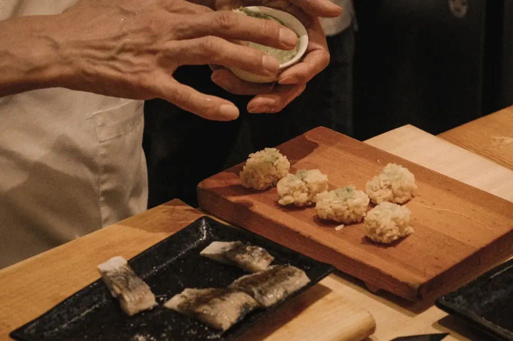 Overhead angled close-up of a sushi chef preparing nigiri and sashimi at Sushi to Sumi counter, demonstrating traditional knife skills, fresh seafood preparation, and authentic omakase dining.