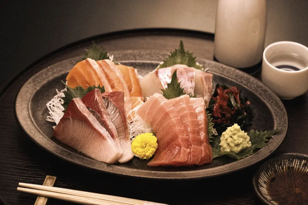 Eye-level three-quarter view of a premium sashimi platter featuring fresh salmon, tuna, and yellowtail sashimi with wasabi, garnishes, and chopsticks in a Japanese restaurant setting.