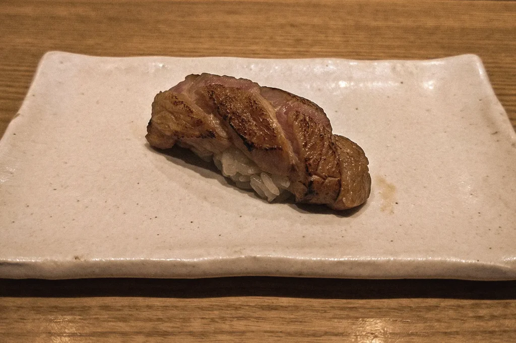 Flame-seared aburi salmon nigiri sushi served on a handcrafted ceramic plate, captured from a three-quarter overhead angle, highlighting the caramelized surface, medium-rare center, and traditional Japanese sushi craftsmanship.