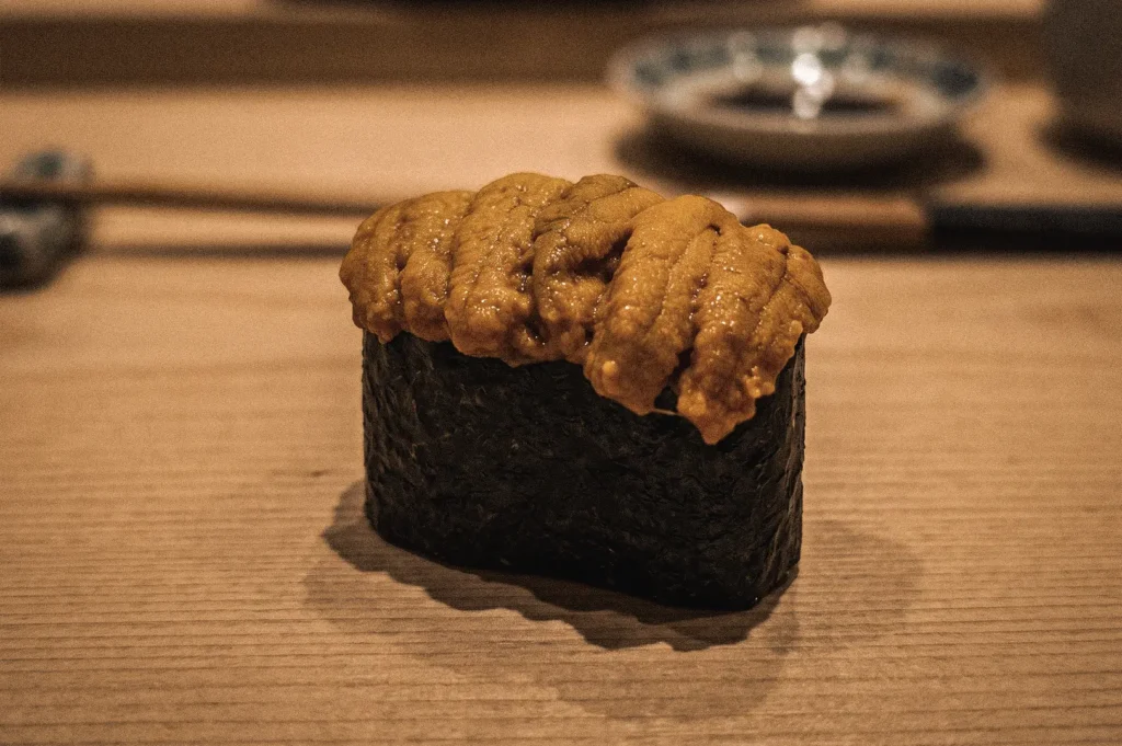 Premium uni gunkan sushi topped with fresh Hokkaido sea urchin and wrapped in crisp nori, photographed from an eye-level macro angle to showcase the signature battleship sushi shape and luxurious uni topping.