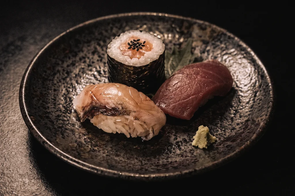 Three-quarter overhead view of nigiri sushi, tuna nigiri, and maki roll served with wasabi, illustrating the difference between nigiri and maki in traditional Japanese sushi cuisine.
