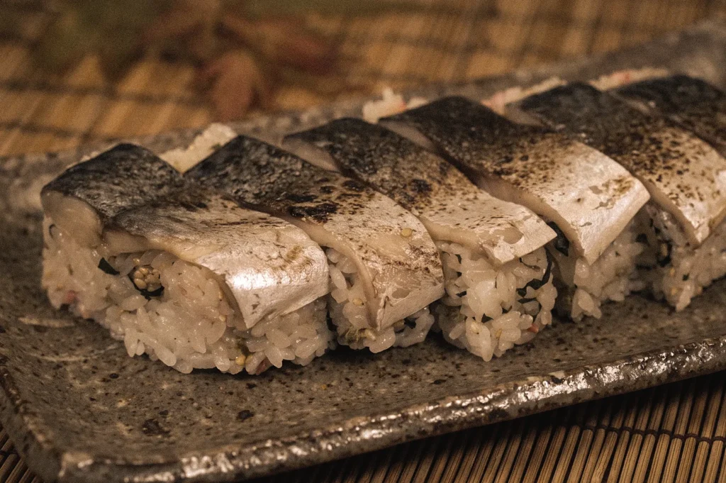 Low-angle three-quarter close-up of battera sushi, traditional Osaka-style oshizushi made with vinegar-cured mackerel pressed over seasoned rice and lightly seared for enhanced flavor.