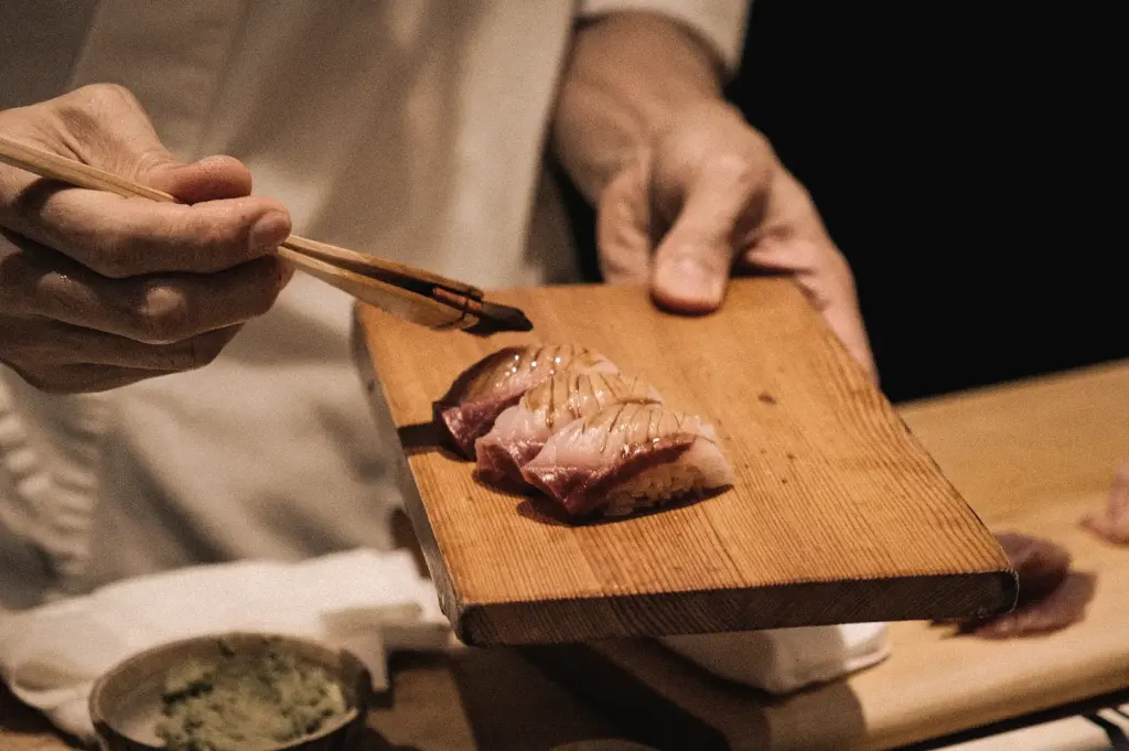 High-angle close-up of a sushi chef serving freshly prepared nigiri on a wooden board, showcasing traditional sushi craftsmanship, premium seafood, and authentic omakase dining.