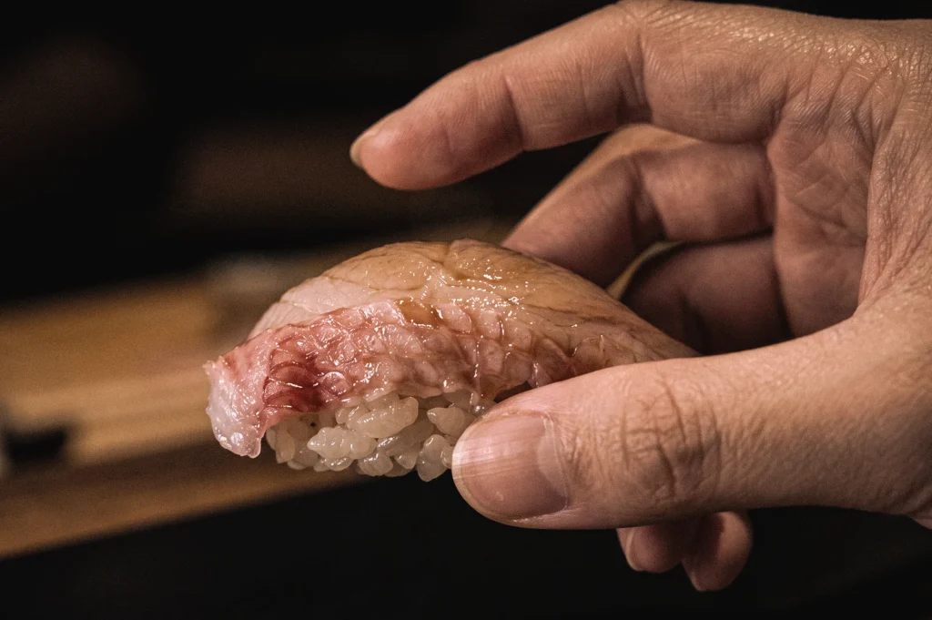 Macro close-up of a hand holding nigiri sushi, demonstrating the traditional way to eat nigiri and showcasing premium seafood over hand-pressed vinegared rice.