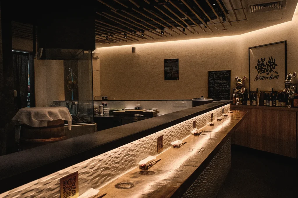 Wide-angle view of a traditional Japanese standing sushi bar with an illuminated counter, showcasing the authentic nigiri sushi dining experience and omakase atmosphere in a modern sushi restaurant.